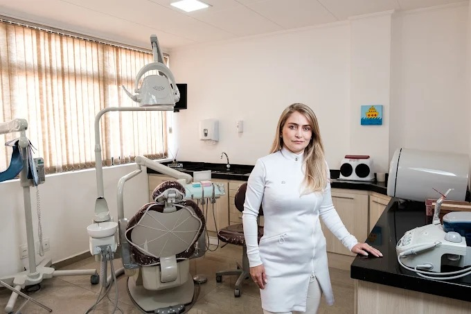 Dra. Carolina ao lado da cadeira odontológica em seu consultório iluminado em Três Corações.